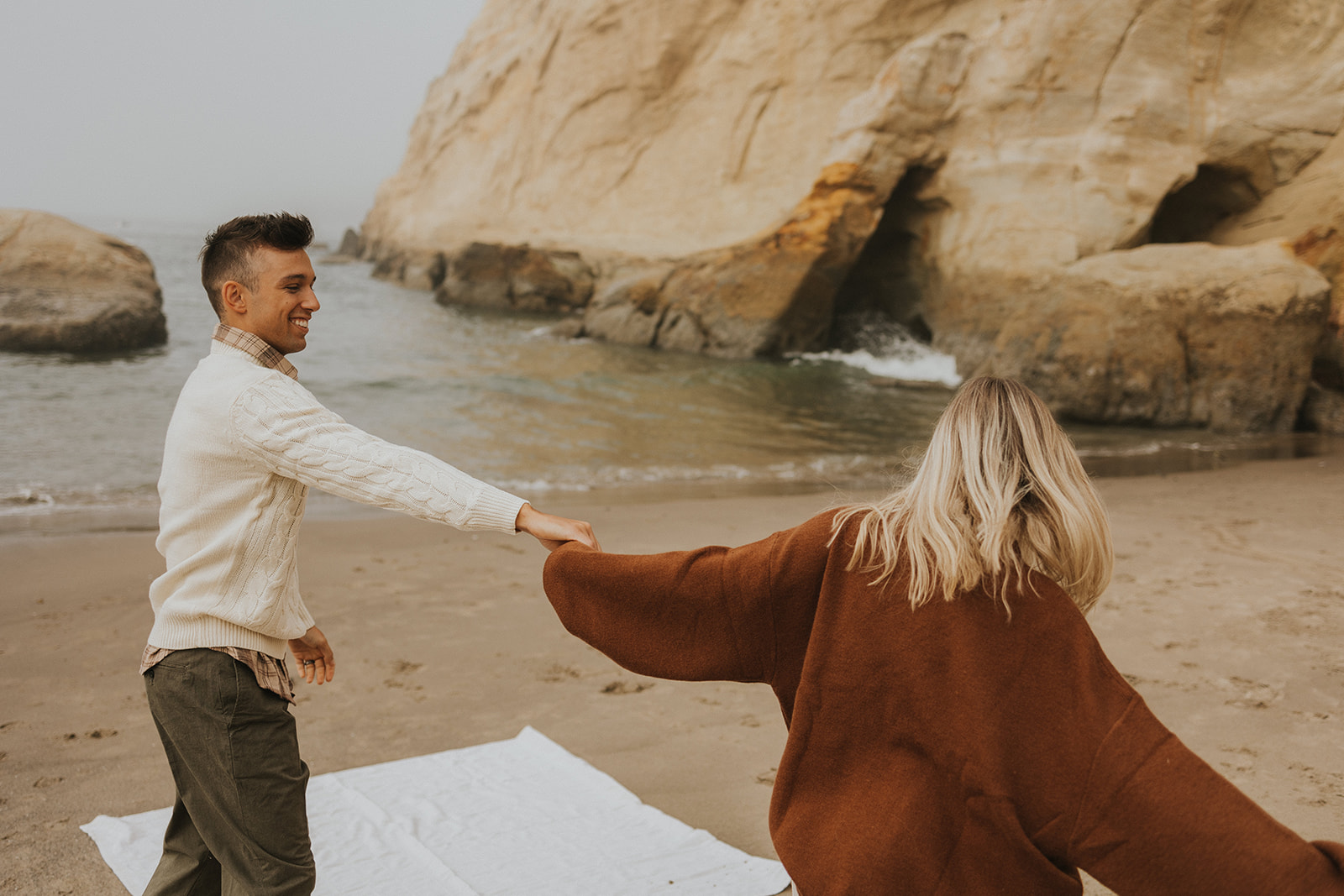 couple holding hands and walking on the beach in oregon Playful Engagement Photos at Cape Kiwanda Oregon