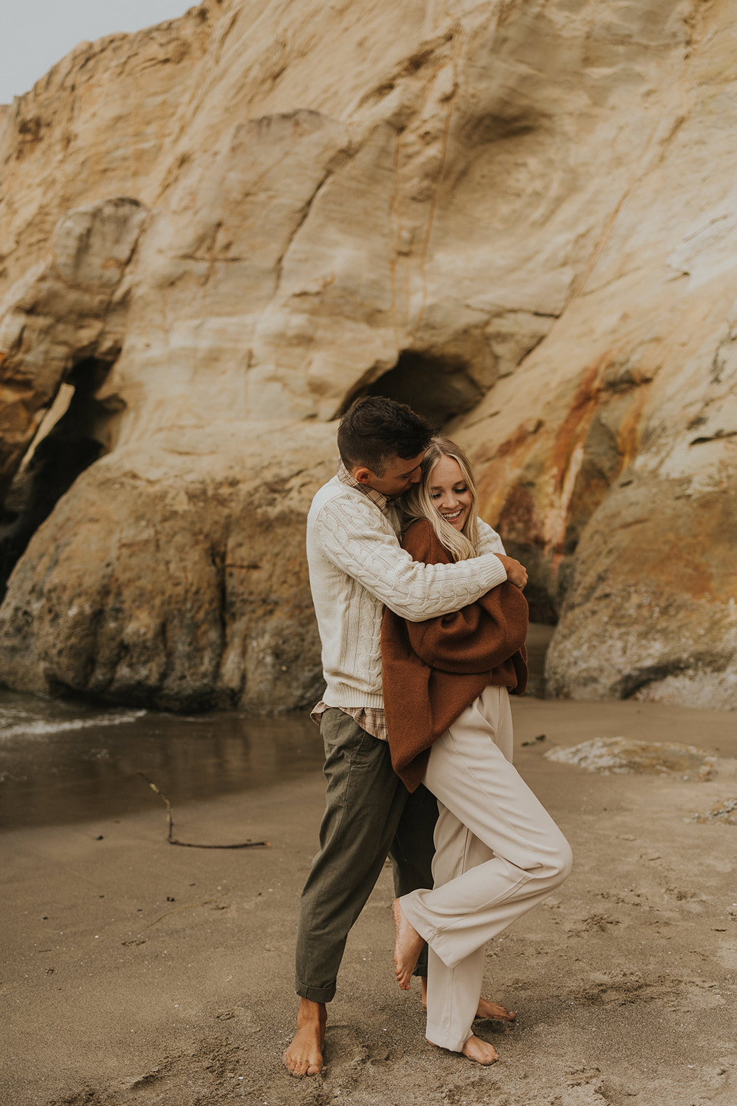 couple hugging on a beach in oregon Playful Engagement Photos at Cape Kiwanda Oregon