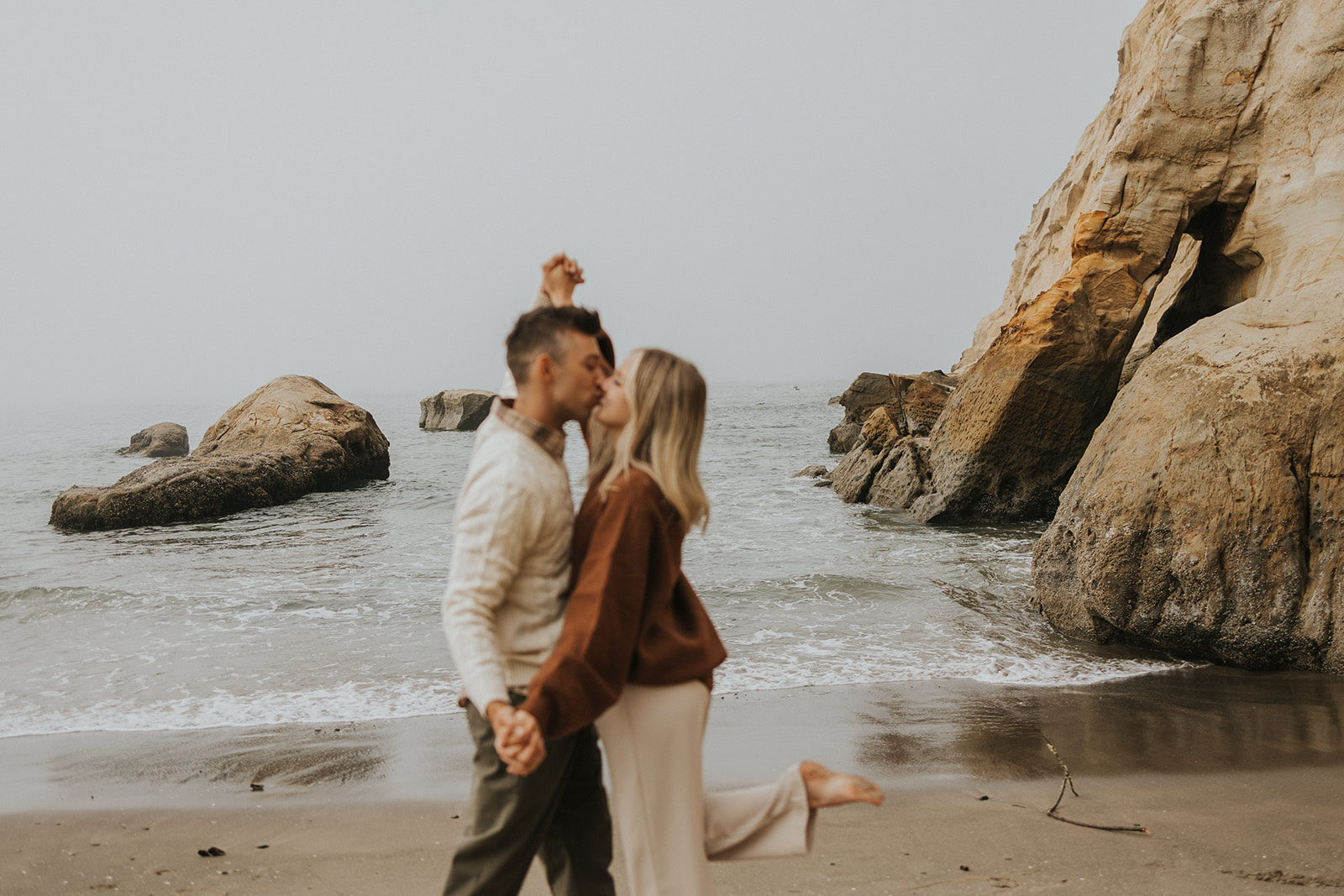 couple holding hands and kissing on a beach in oregon