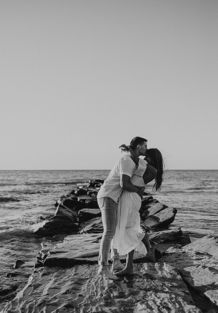 Couple kissing on beach rocks for engagement photoshoot
