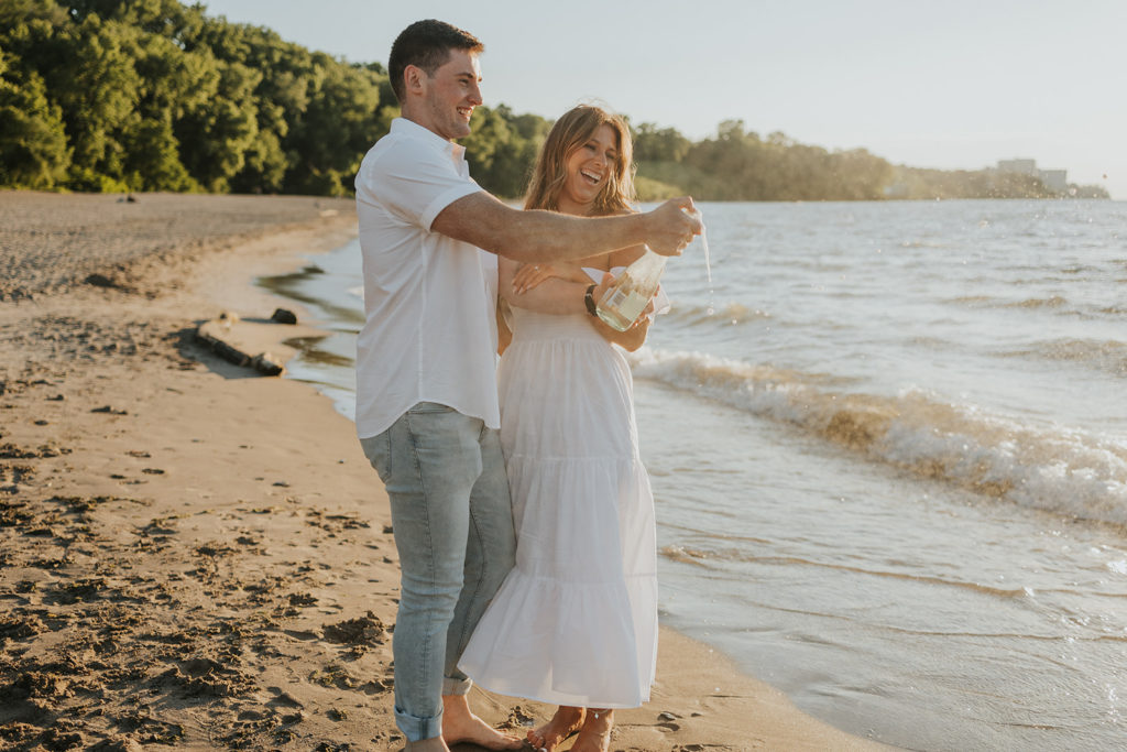 Couple opening bottle of champagne during their engagement photoshoot beach session