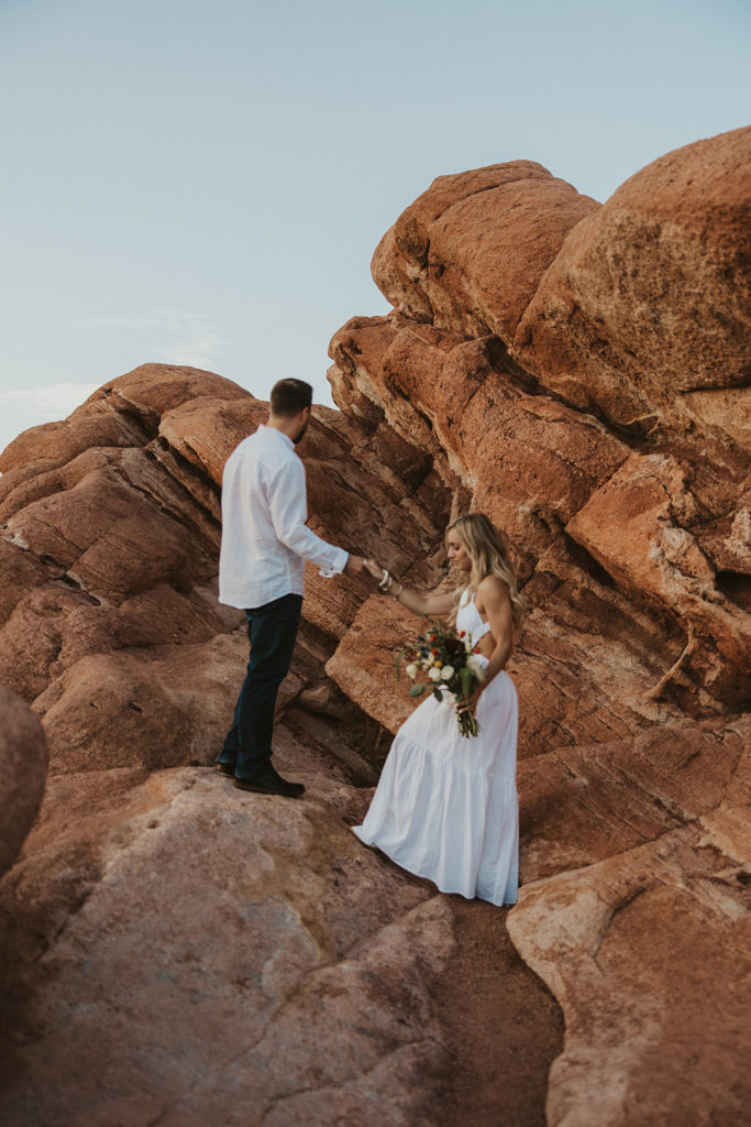Newly weds climbing mountain rocks during photoshoot 