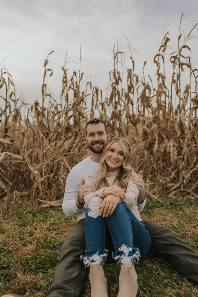 Newly engaged couple sitting in a field for engagement photos