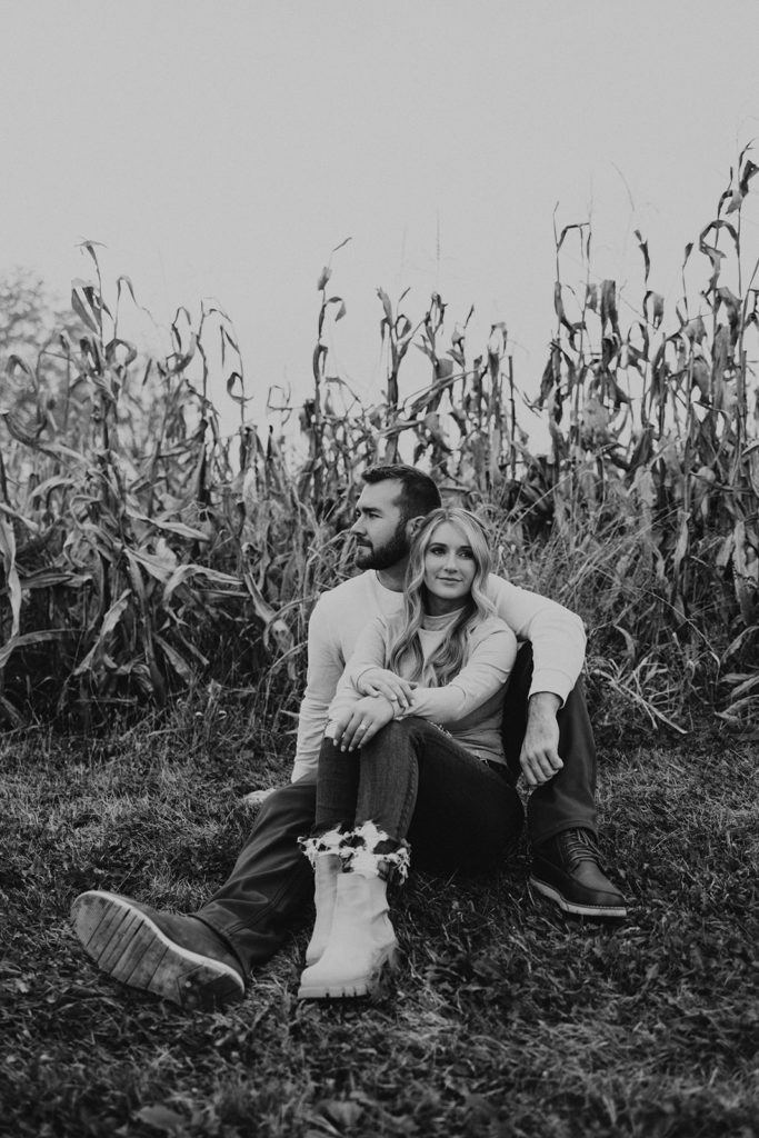 Black and white engagement photo of couple sitting in Ohio cornfields