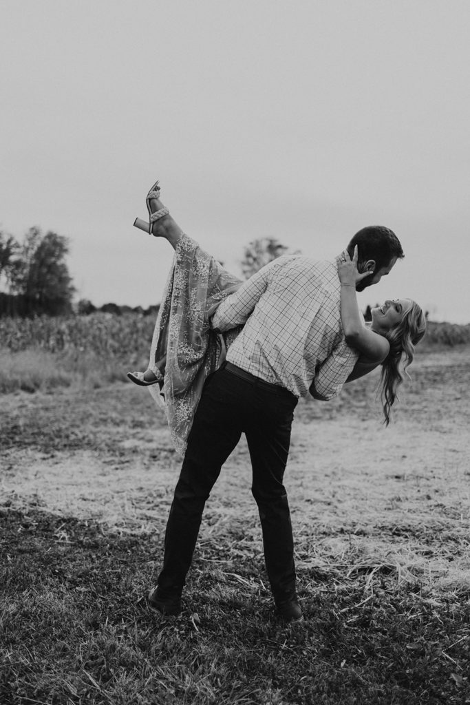 Man holding woman for fall field engagement photos in a black and white picture 