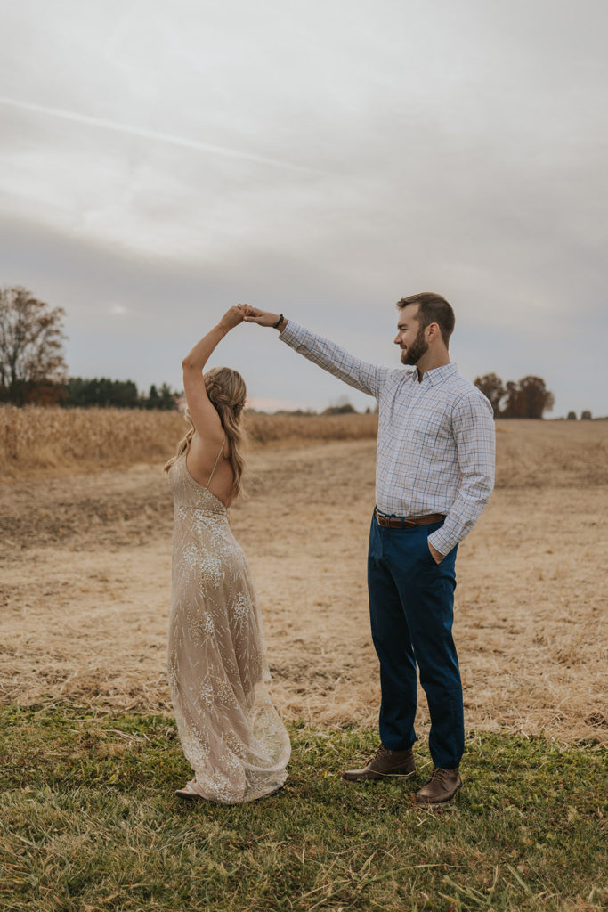 Man twirling woman around for fall field engagement photos 