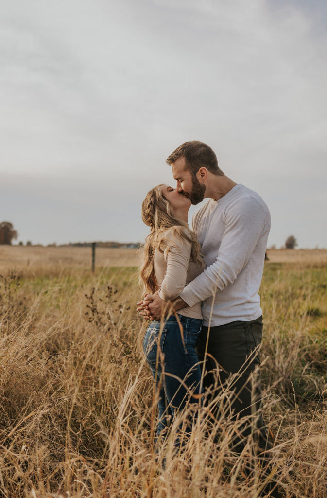 Newly engaged couple kissing in field for engagement photoshoot
