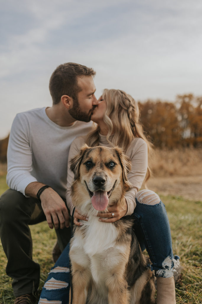 Newly engaged couple kissing for engagement photoshoot with a dog