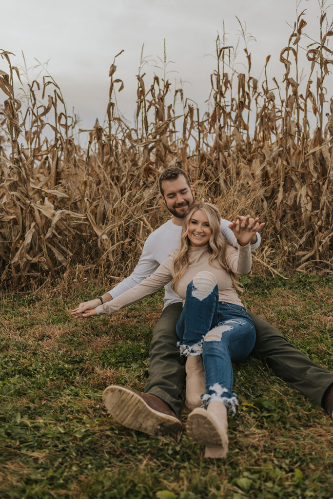 Man and woman sitting in front of cornfield for fall engagement photos