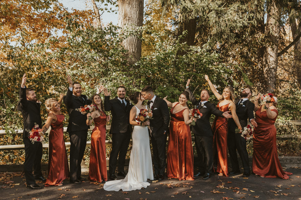 The entire bridal party posing while bride and groom kiss