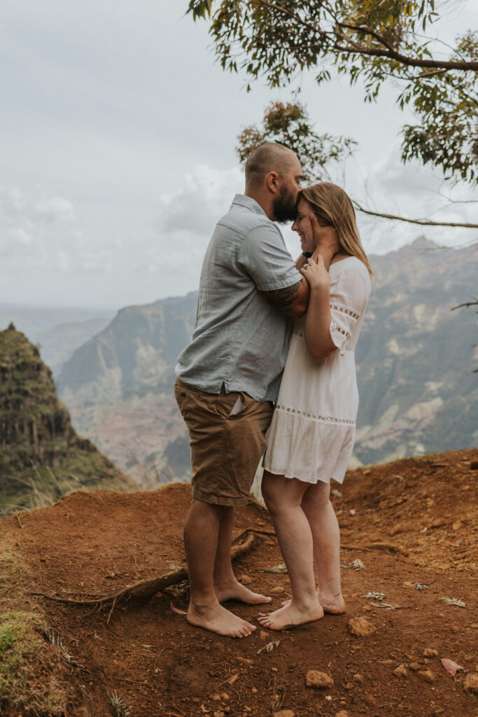 husband kissing his wife's forehead with the Waimea Canyon in the background
